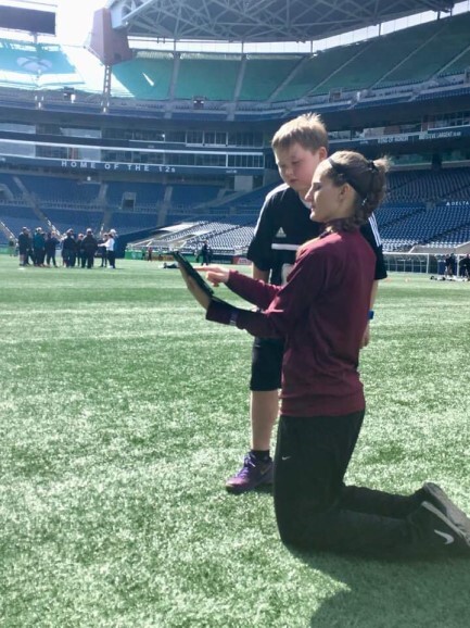 A TRG referee mentor kneels on the pitch to guide a young official